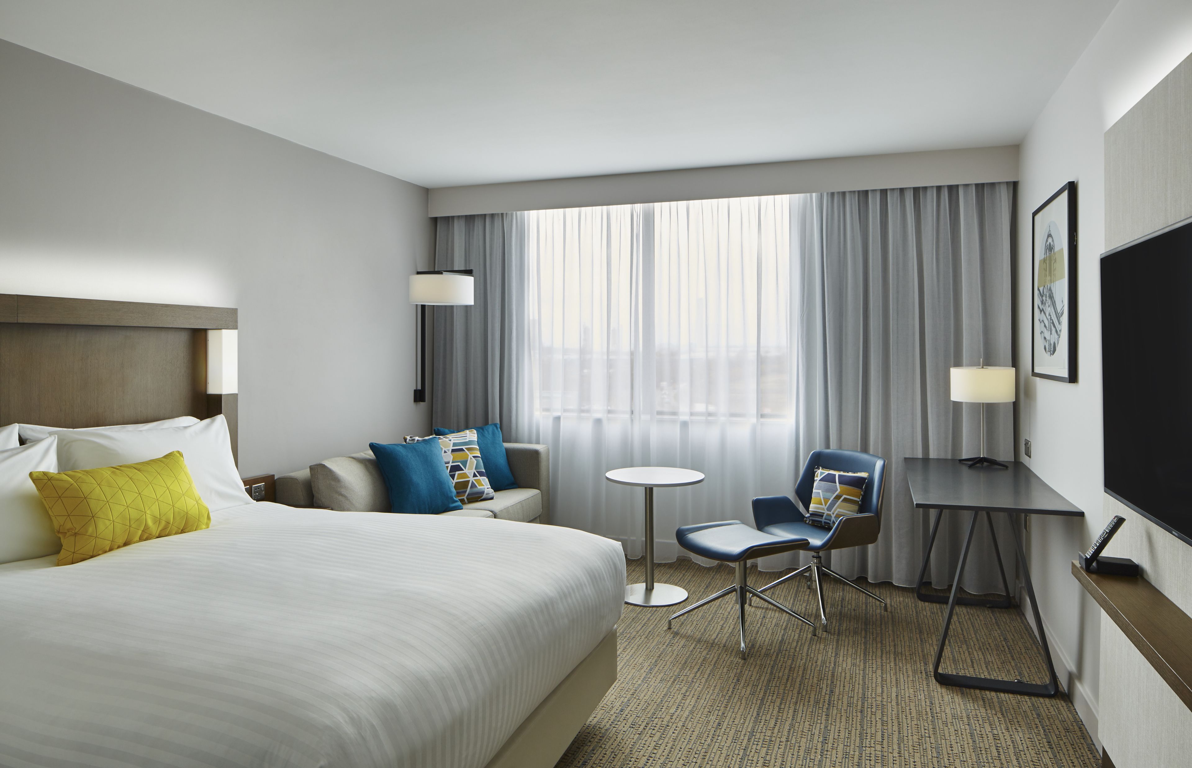 Une chambre d’hôtel avec un grand lit, un bureau, une chaise, une petite table et un téléviseur.