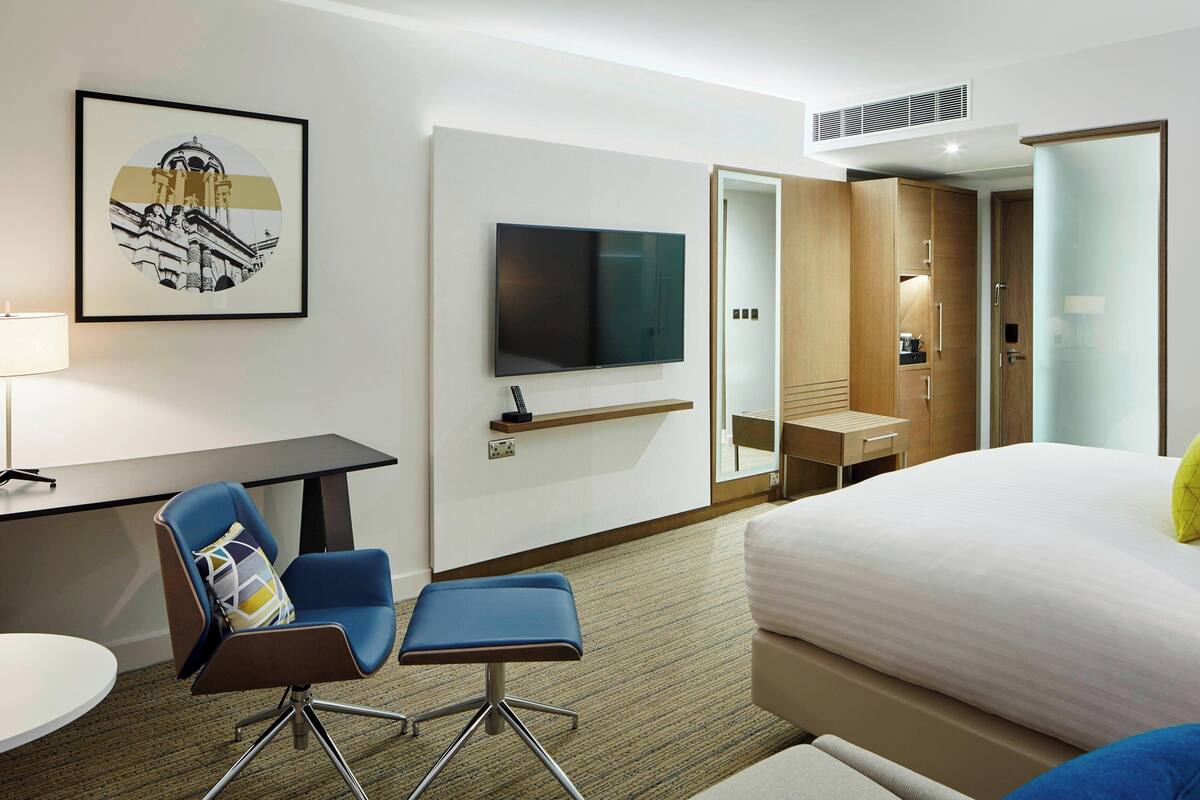 Una habitación de hotel con cama, escritorio, silla, televisor y armario.