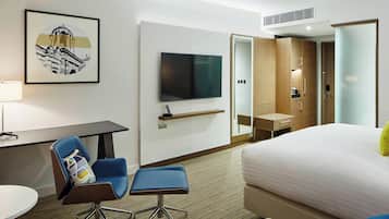 A hotel room with a bed, a desk with a chair, a television, and a wardrobe.