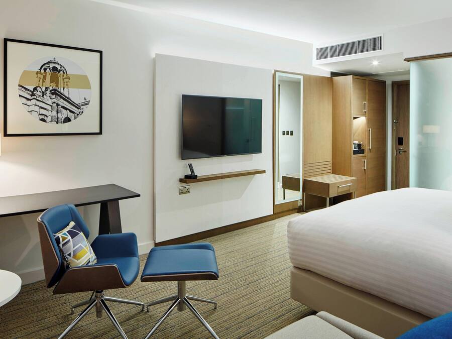 A hotel room with a bed, a desk with a chair, a television, and a wardrobe.