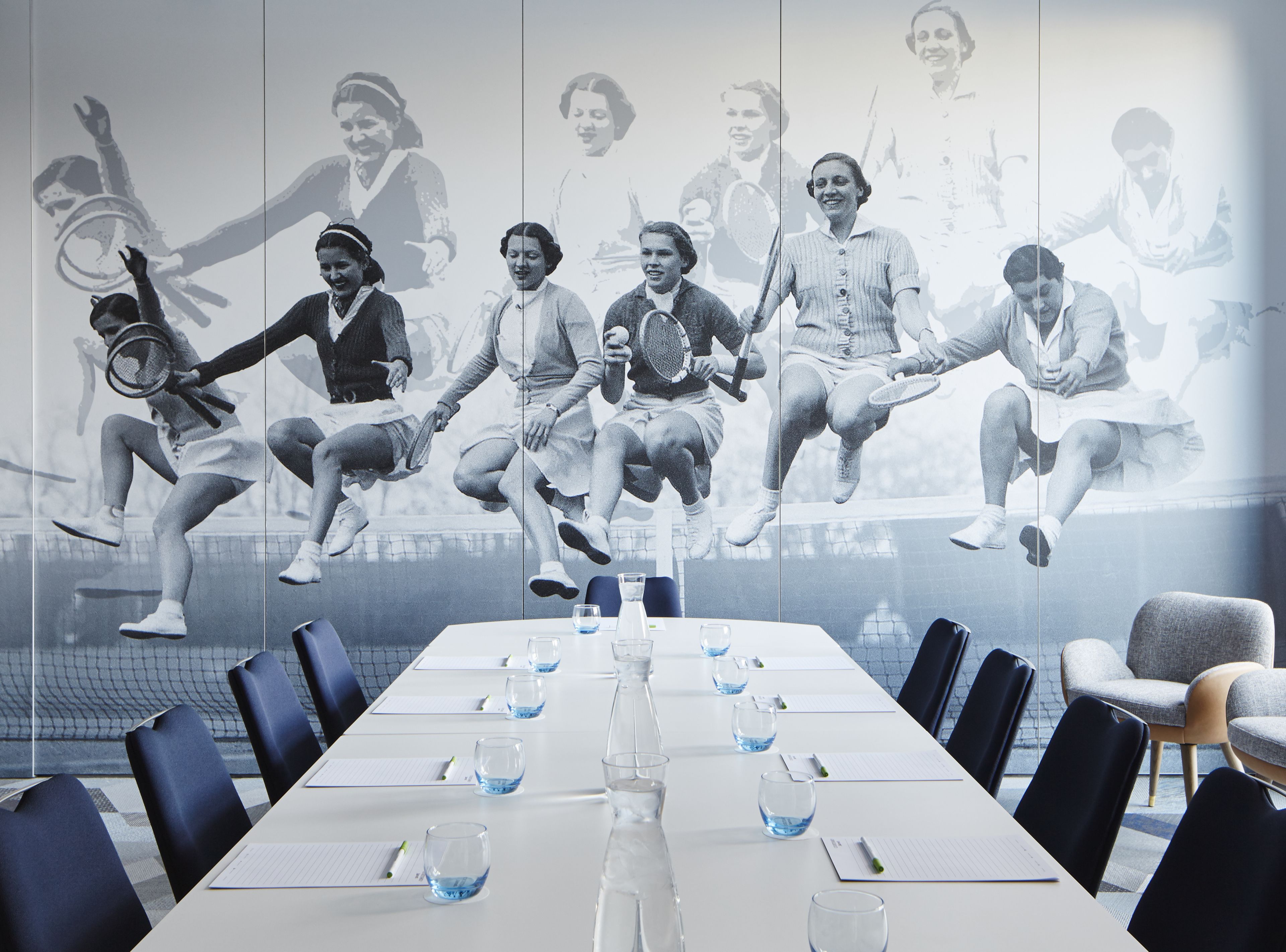 A conference room with a long table, chairs, and a large wall mural of tennis players.