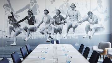 A conference room with a long table, chairs, and a large wall mural of tennis players.