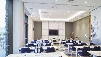 Une salle de conférence équipée de tables, de chaises et d’un grand écran.