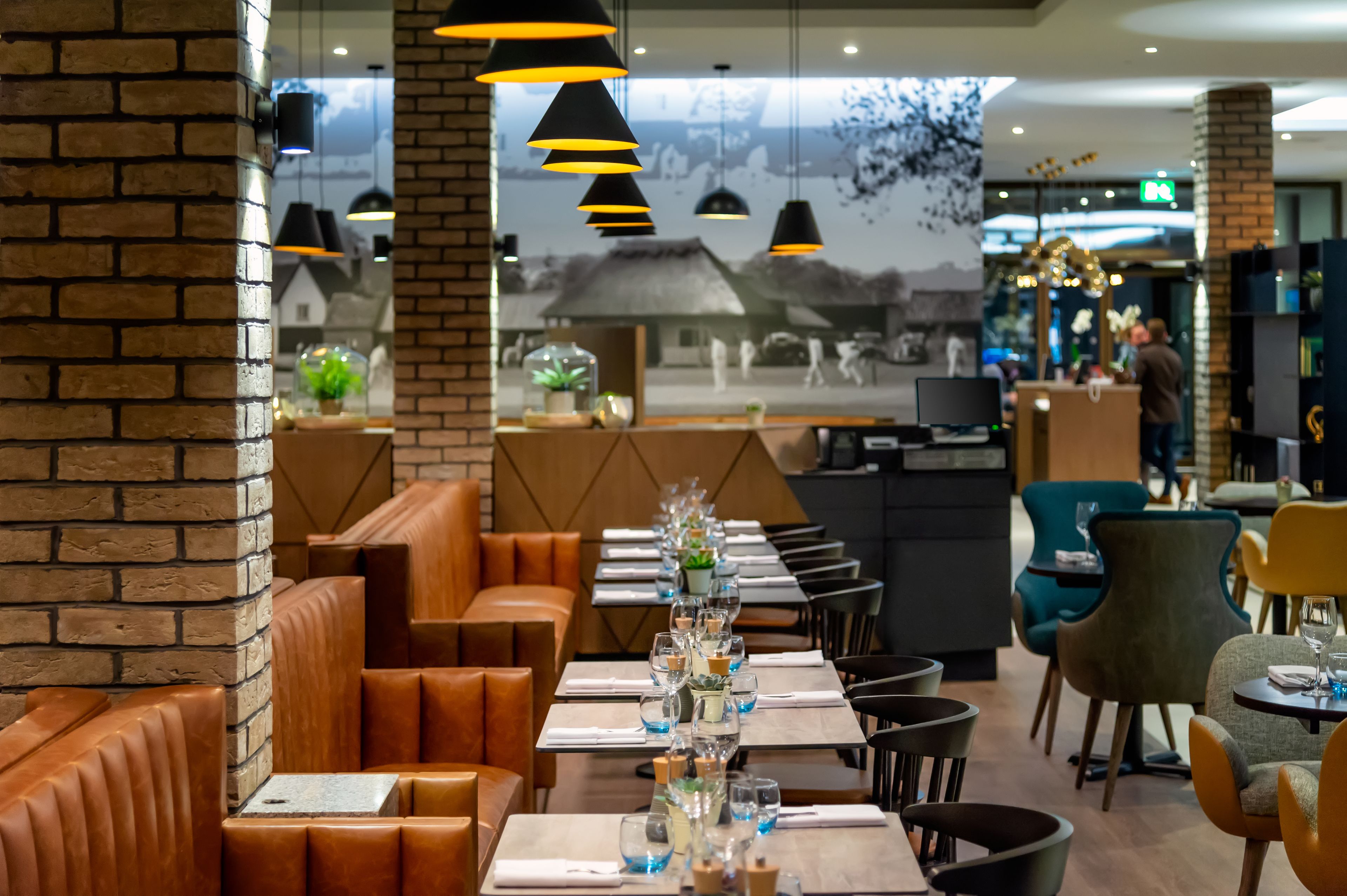 A restaurant with brick walls, leather booths, and a long table set with glasses and a centerpiece.
