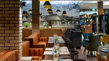 A restaurant with brick walls, leather booths, and a long table set with glasses and a centerpiece.