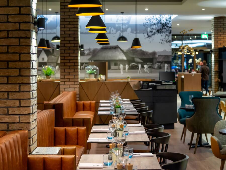 A restaurant with brick walls, leather booths, and a long table set with glasses and a centerpiece.