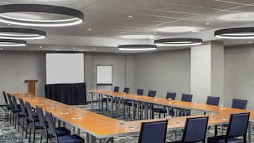 Un salón de conferencias con una larga mesa, sillas, una pantalla de proyector y un atril.