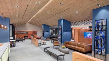 A spacious lobby with a high ceiling, a brick fireplace, seating areas, and a TV screen.