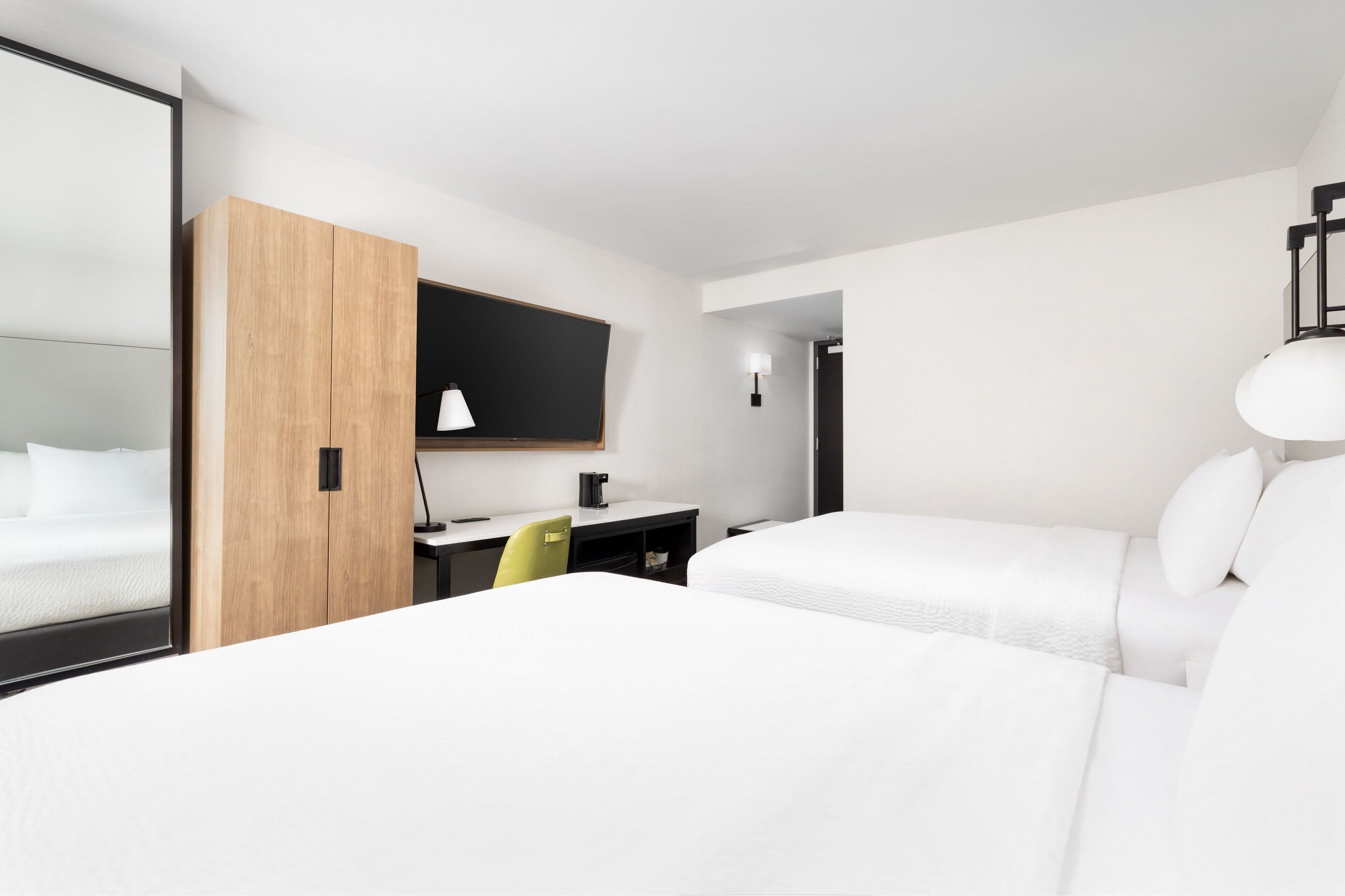 A hotel room with two beds, a desk, a chair, and a mirror.