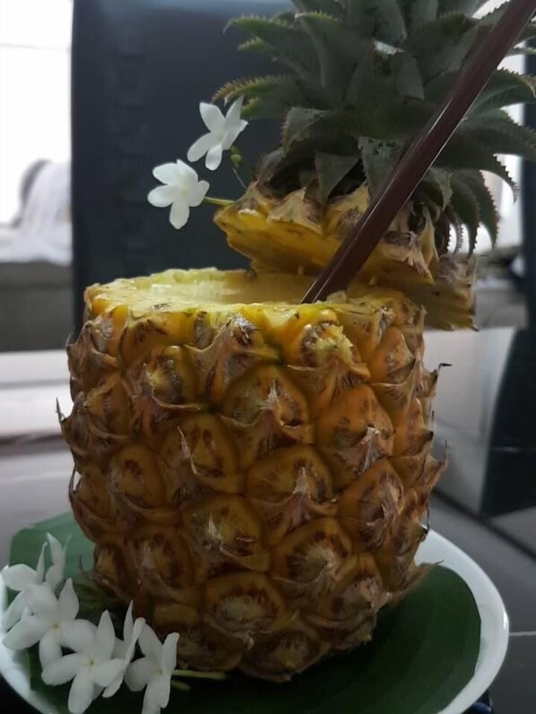Una piña con una pajita sobre un plato verde, rodeada de flores blancas.