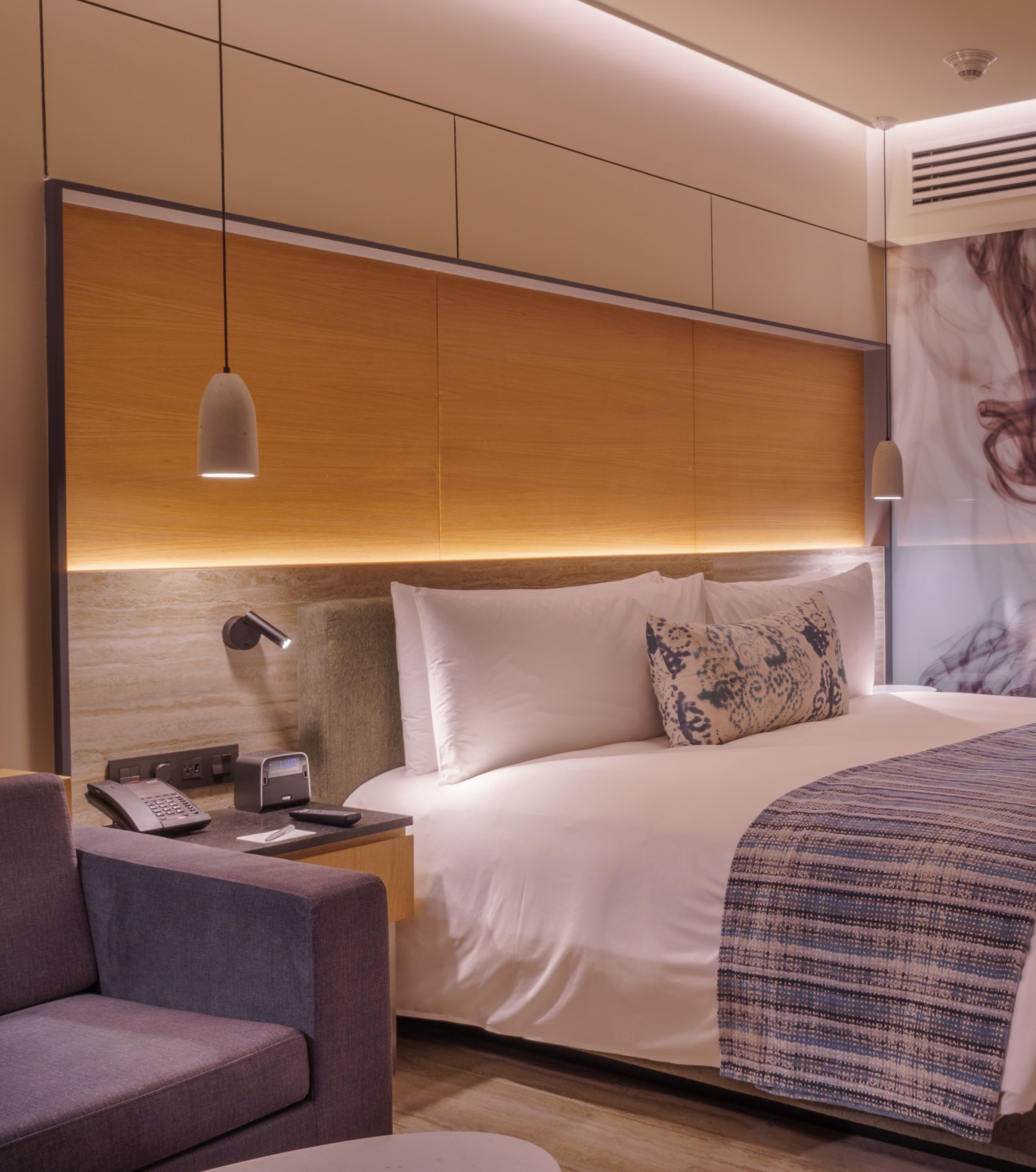 Una camera d'albergo moderna con un letto grande, una scrivania con telefono e laptop, una sedia e un'ampia opera d'arte appesa al muro.