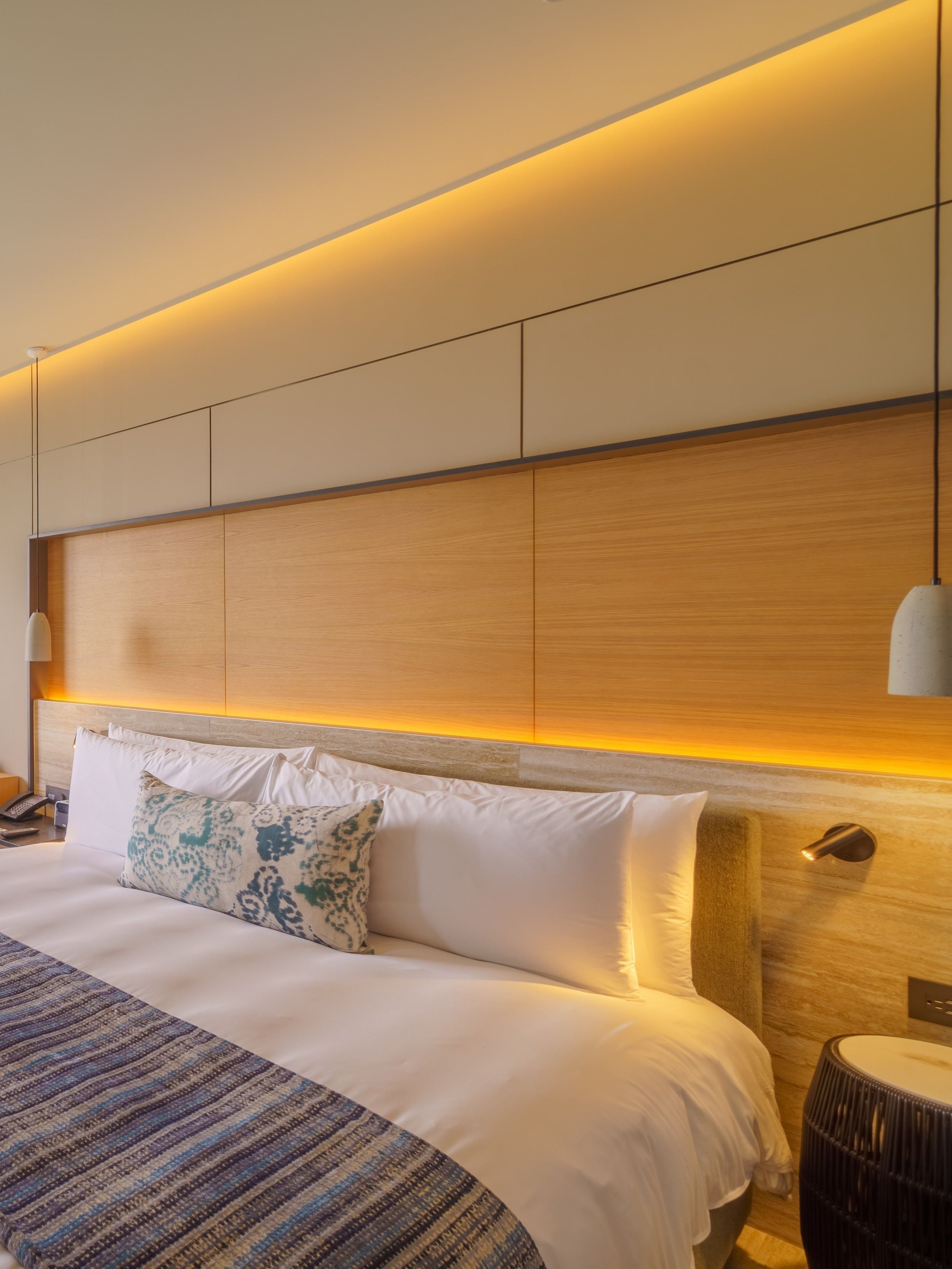 A modern hotel room with a large bed, a wooden headboard, and a bedside lamp.