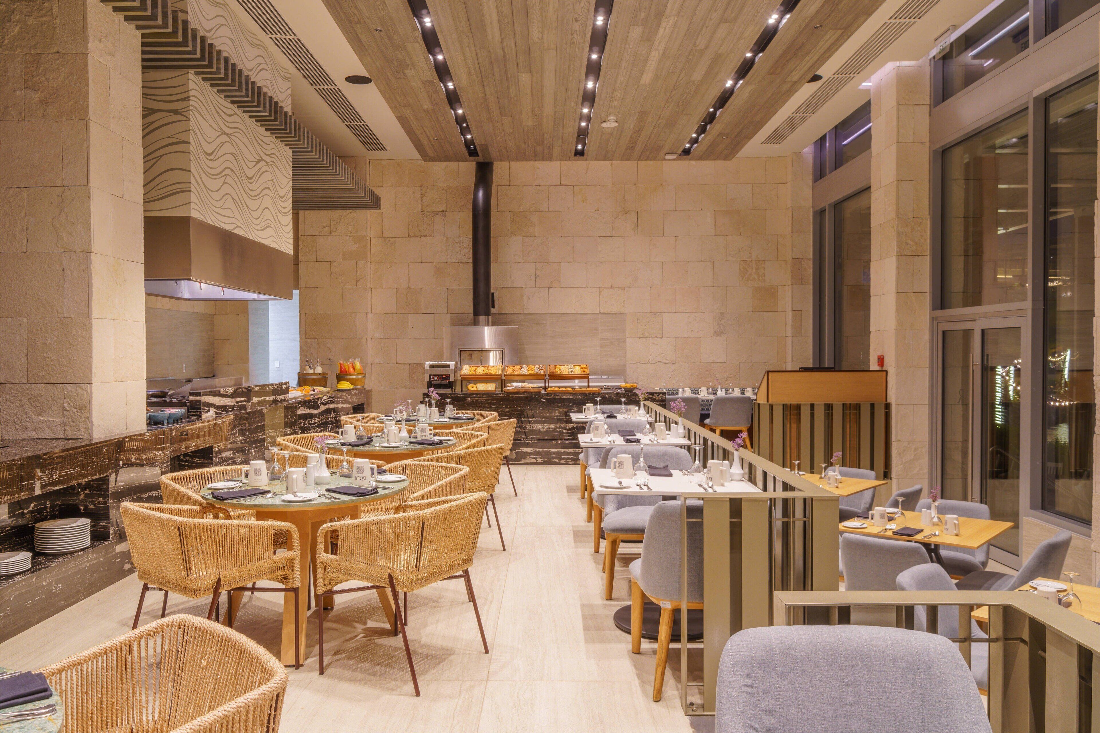 A modern restaurant with a long counter, wicker chairs, and a stone-tiled floor.
