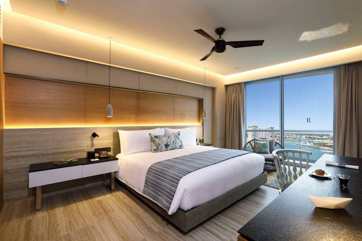 A modern hotel room with a large bed, bedside tables, a desk, and a view of the city.