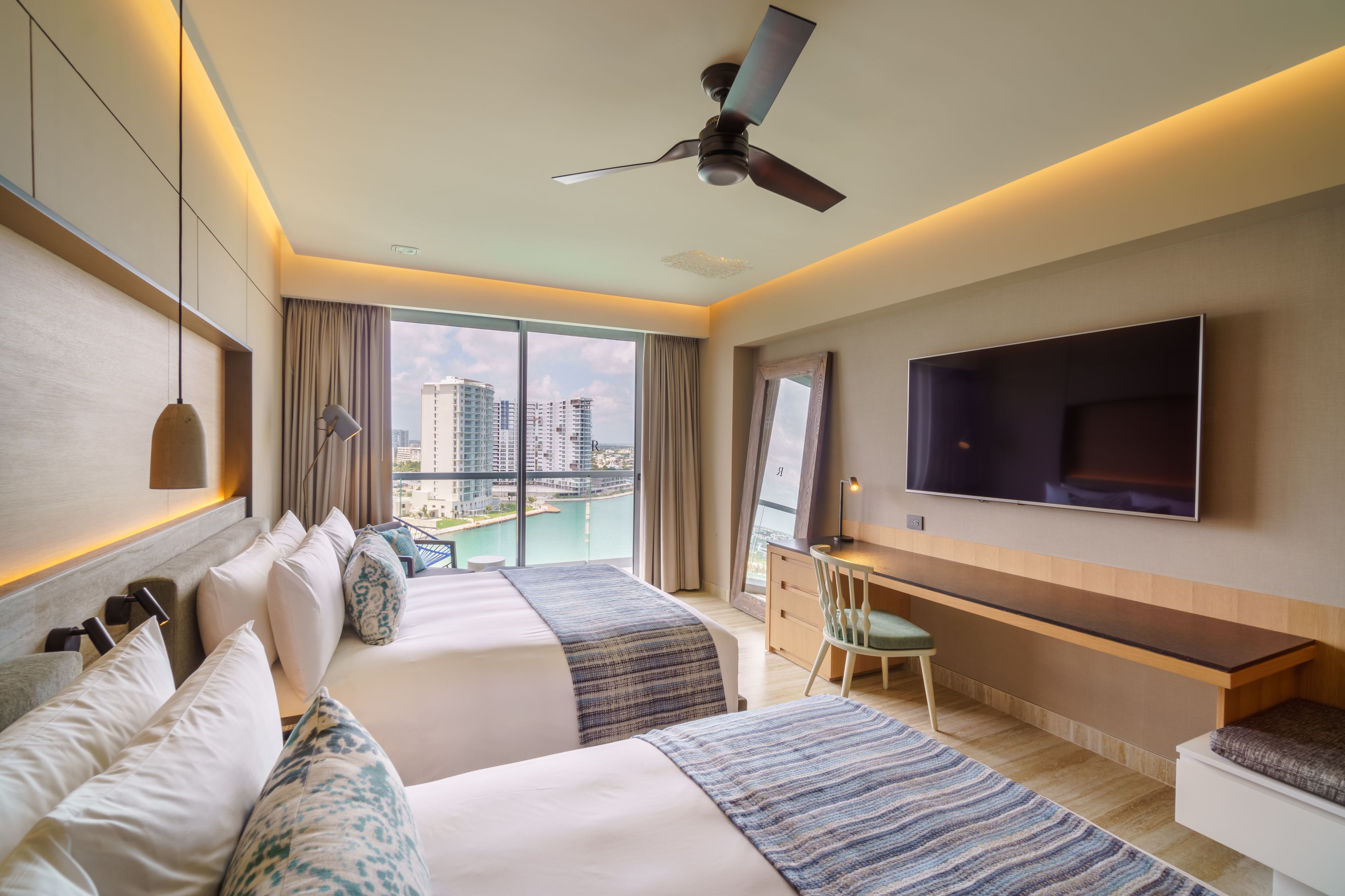 Une chambre d’hôtel moderne avec deux lits, un bureau, une chaise, une télévision et une vue sur la ville.