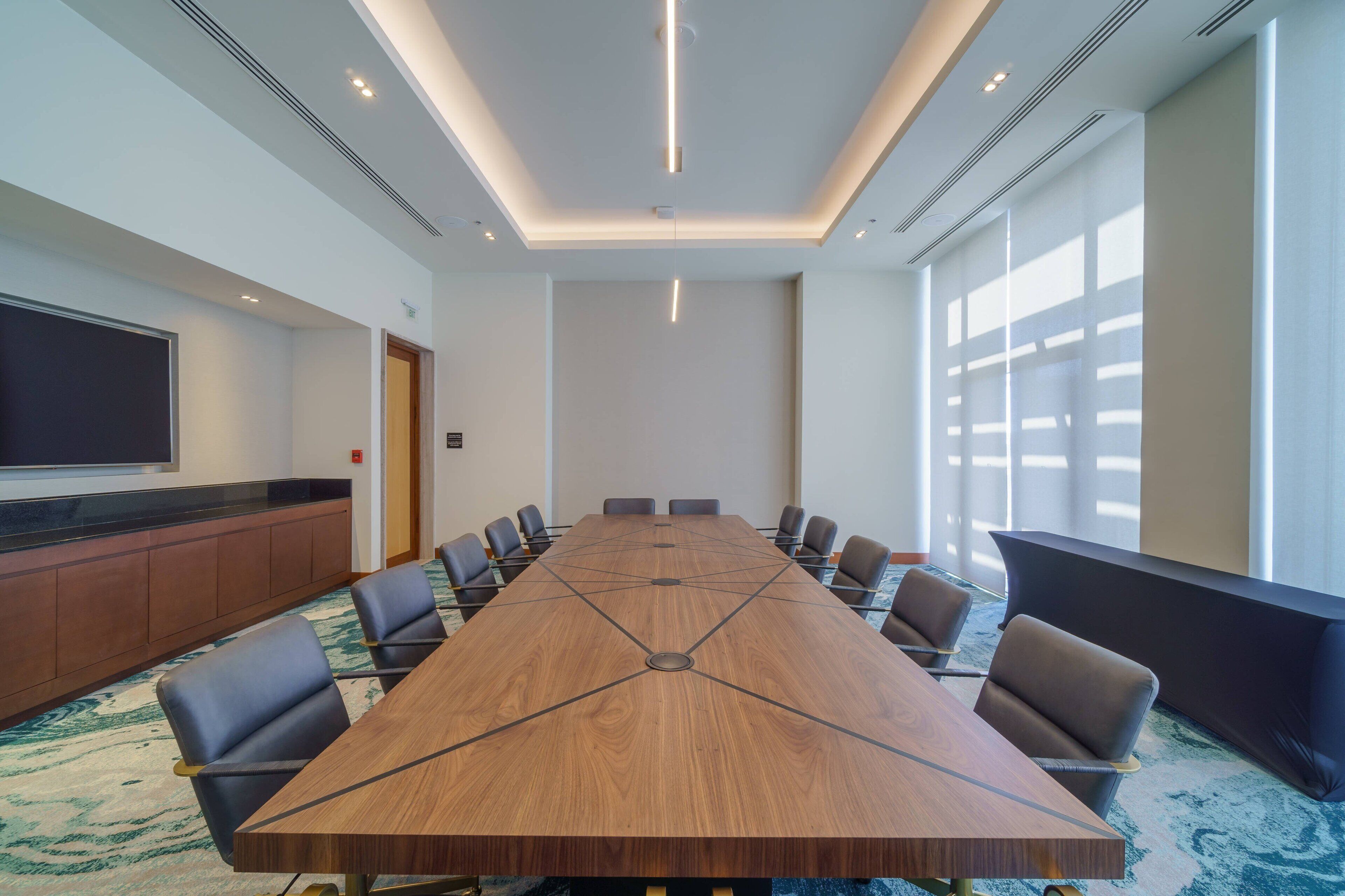 A conference room with a long table, chairs, a TV screen, and a carpeted floor.