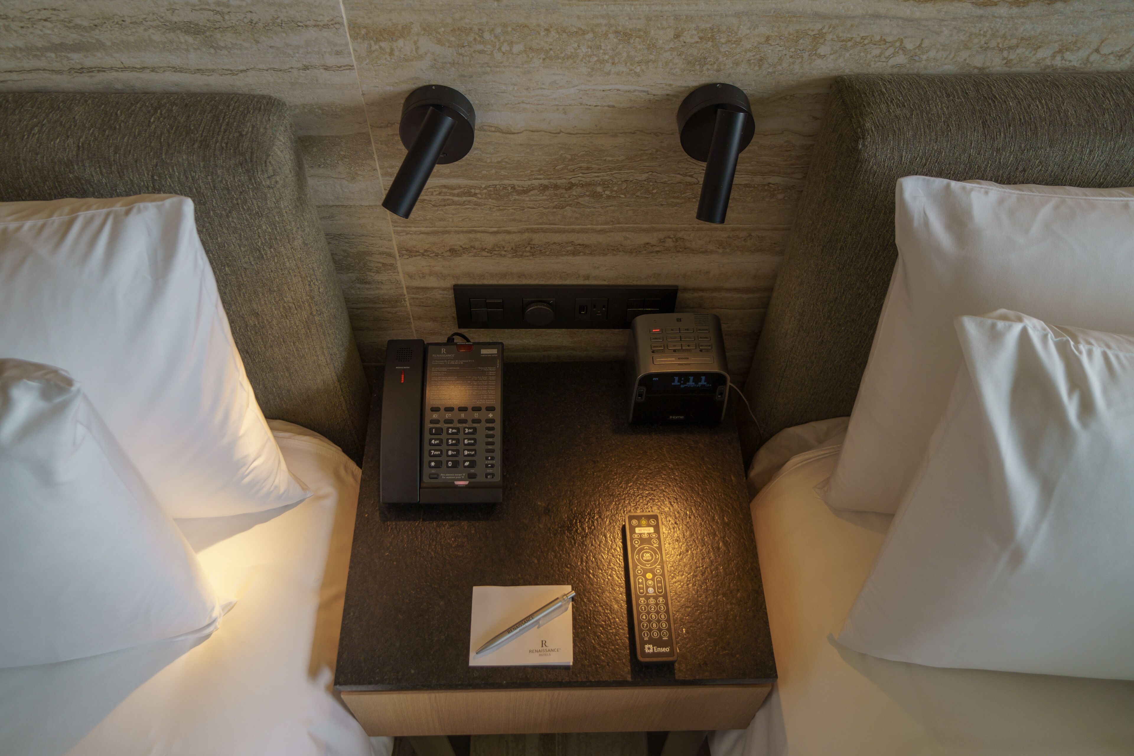 Una habitación de hotel con una mesita de noche que tiene un teléfono, un control remoto y un bolígrafo.