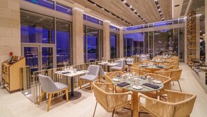 A modern restaurant with high ceilings, large windows, and wicker furniture. - Renaissance Cancun Resort & Marina (Cancún)
