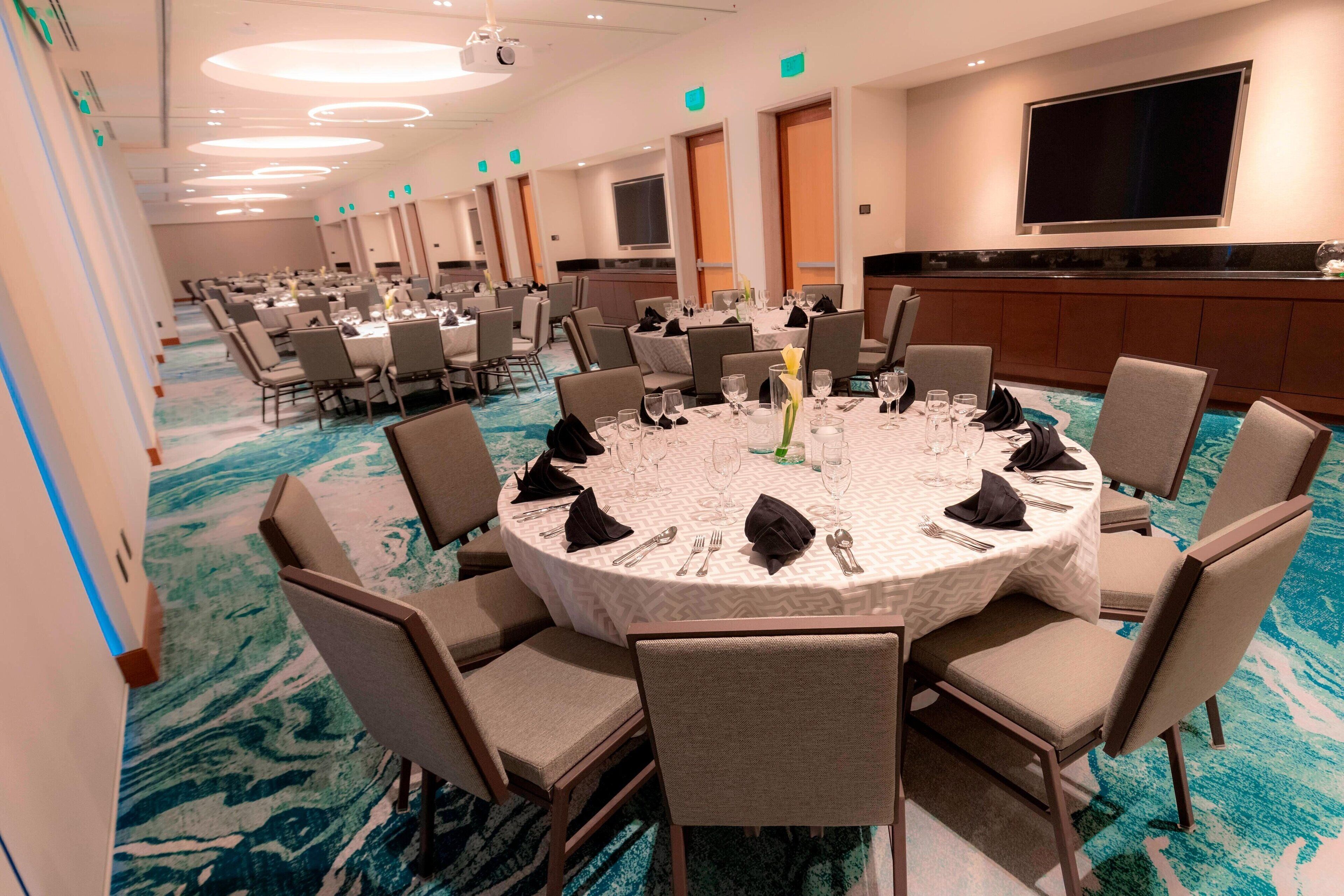 A conference room with round tables, chairs, and a large screen on the wall.