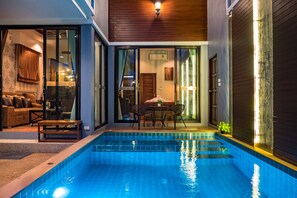 A modern indoor pool area with a glass door entrance, a seating area with a table and chairs, and a wooden ceiling. - KG Private Pool Villas Soi Nine (Krabi)