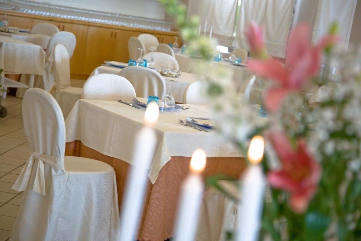 A restaurant with round tables covered in white tablecloths, chairs with white covers, and candles on the tables.