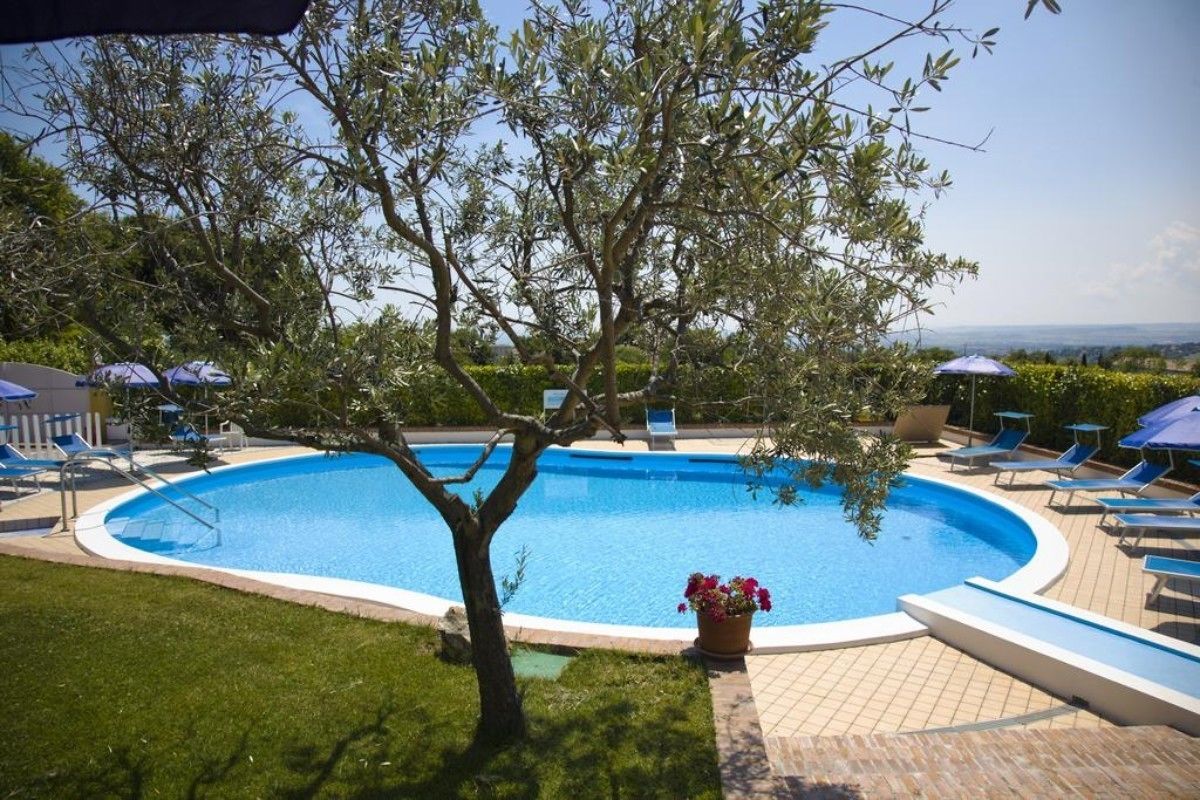 Una piscina circular con sillas de descanso y sombrillas, rodeada de follaje y vistas al paisaje.