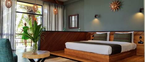 A bedroom with a wooden bed, a small round table, a green chair, and a large window with curtains.