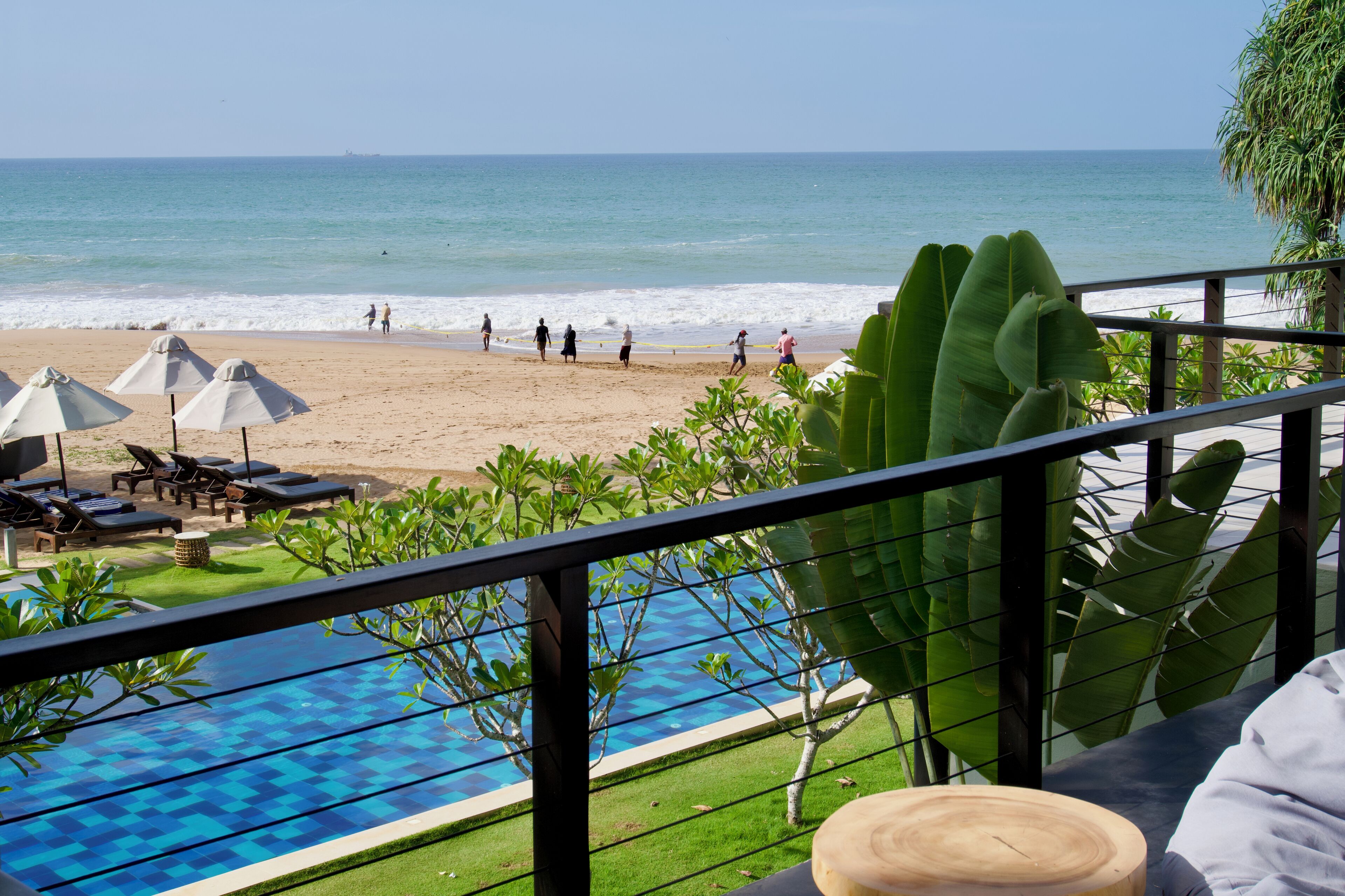 A poolside view with a beach and ocean in the background.