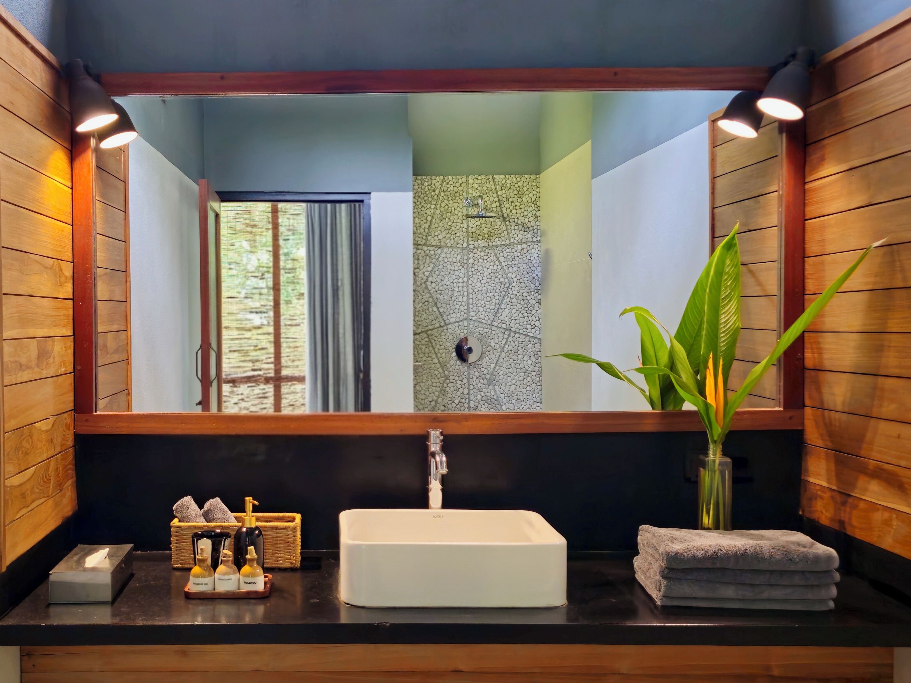 A bathroom with a large mirror, wooden walls, a white sink, and a plant.