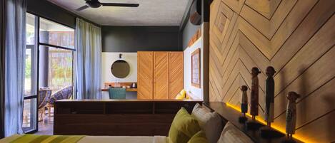A hotel room with a bed, a desk, a chair, a ceiling fan, and a view of the outside.