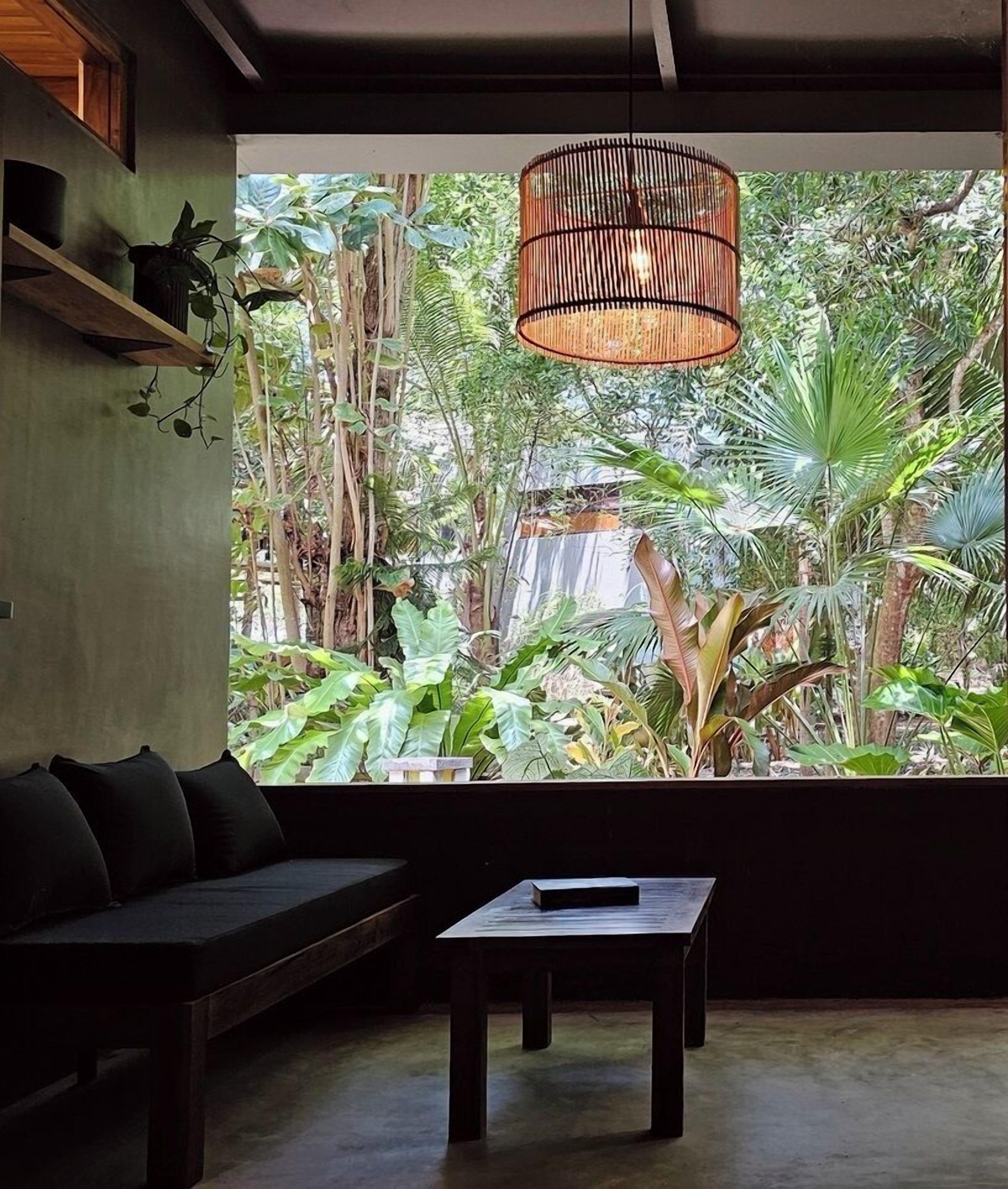 Una habitación con un ventanal grande, un sofá negro, una mesita y una lámpara colgante.