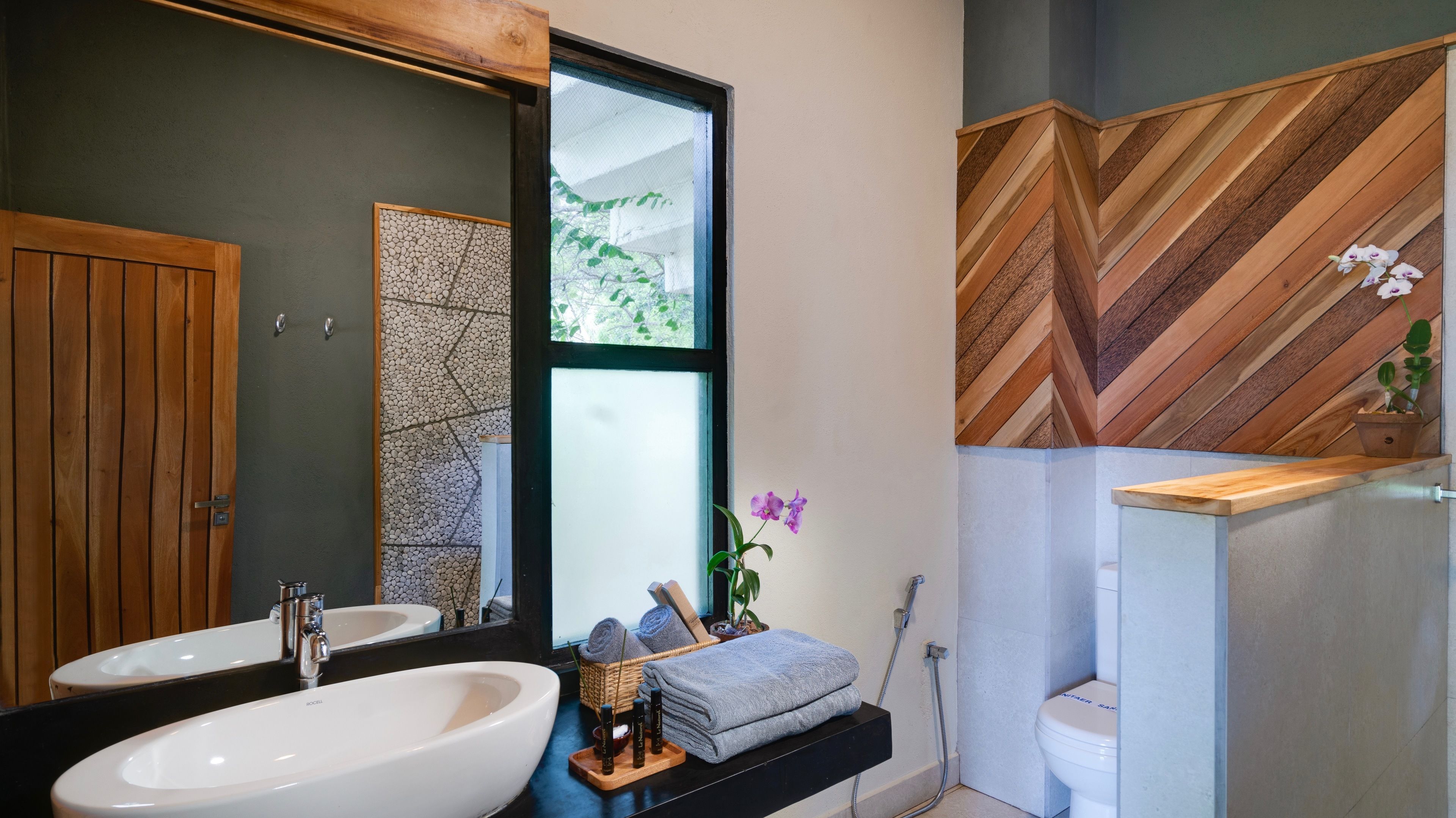 A modern bathroom with a large mirror, two sinks, a wooden door, and a herringbone-patterned wall.