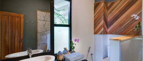 A modern bathroom with a large mirror, two sinks, a wooden door, and a herringbone-patterned wall.