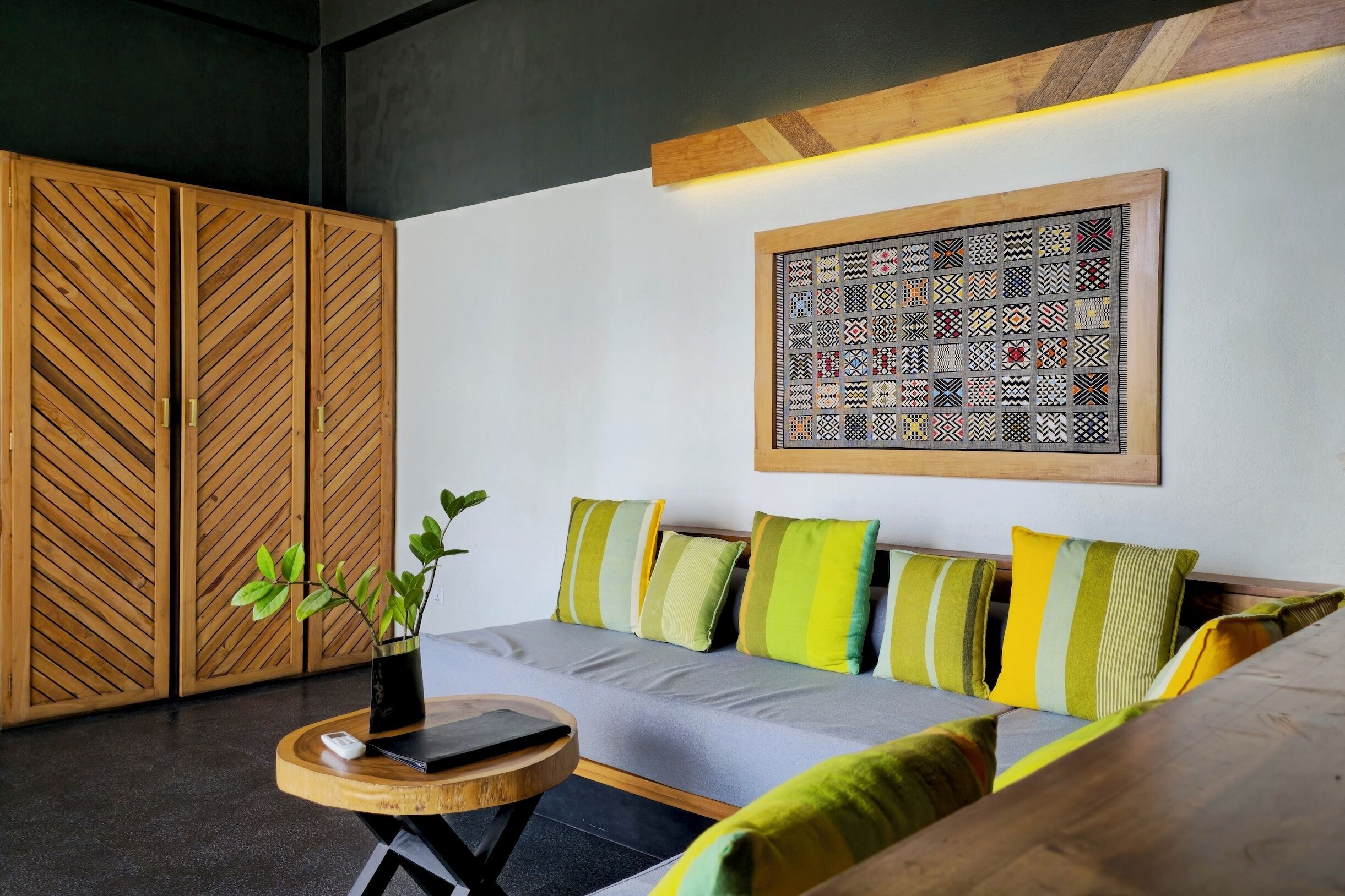 Une pièce moderne avec un canapé gris, des coussins à rayures, une table d’appoint en bois ornée d’une plante, et une œuvre d’art abstraite encadrée accrochée au mur.