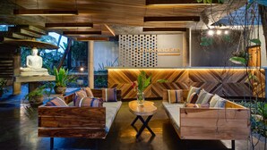 A modern lounge area with wooden furniture, a Buddha statue, and a herringbone-patterned wall. - Lankavatara Ocean Retreat & Spa (Kalametiya)