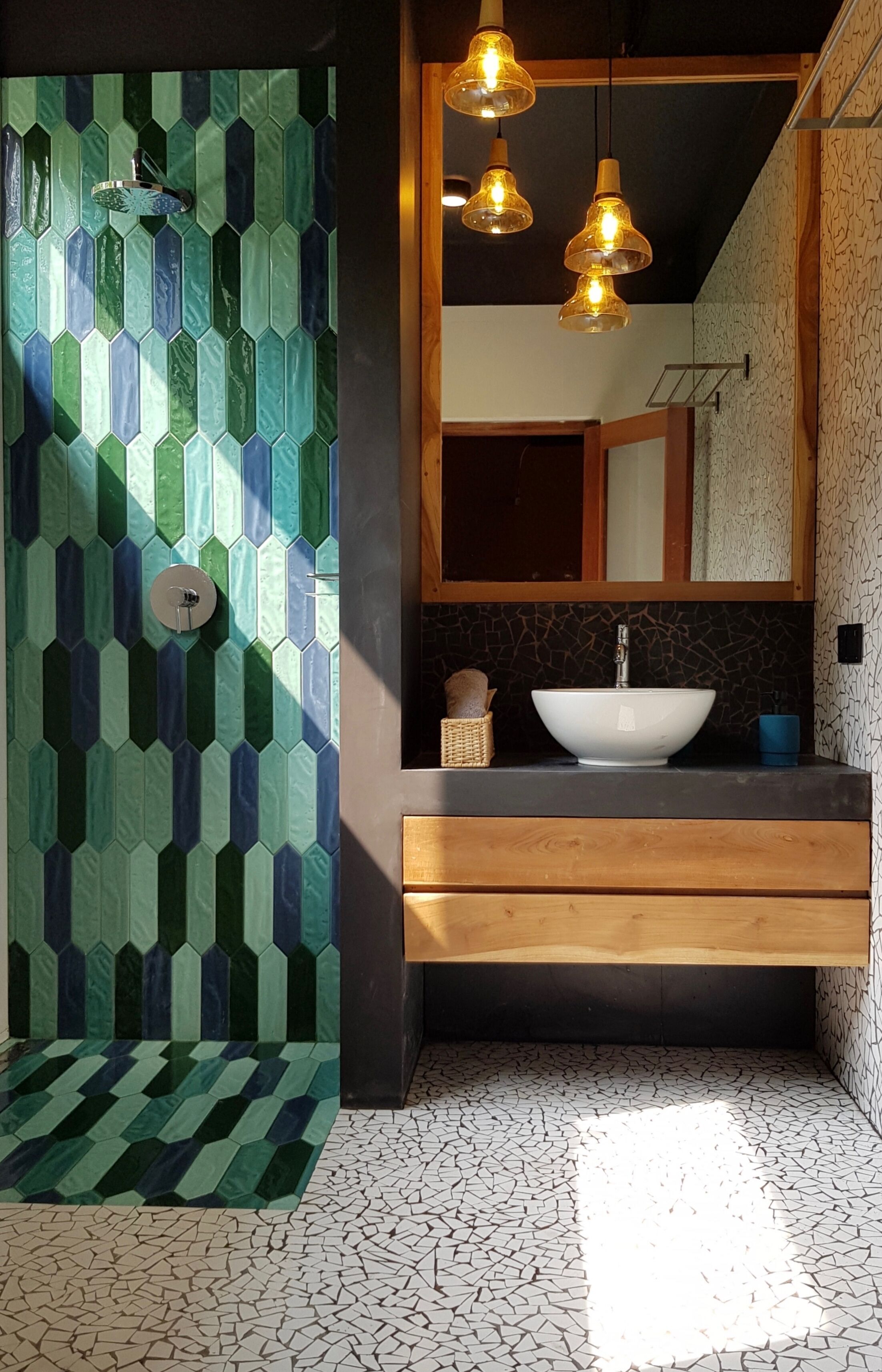 A bathroom with a hexagonal tile wall, a white sink, wooden vanity, and pendant lights.