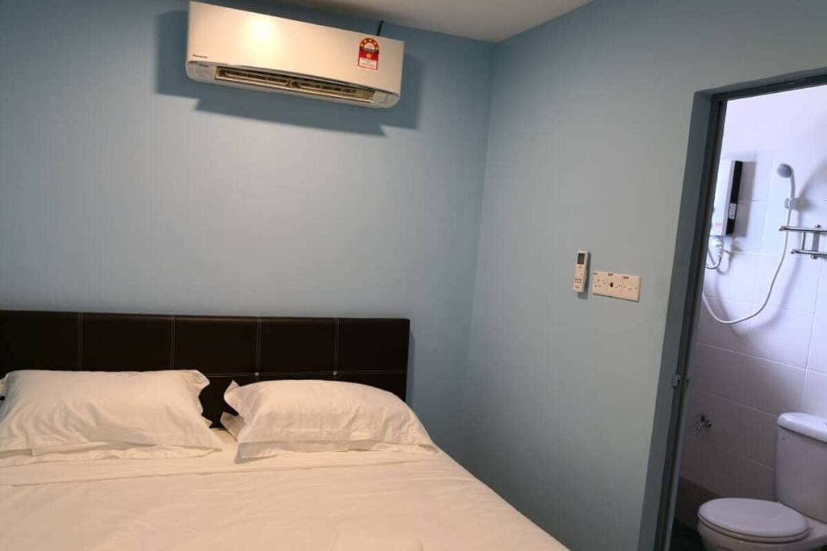 A hotel room with a bed, an air conditioner, a phone, and a bathroom with a toilet and shower.