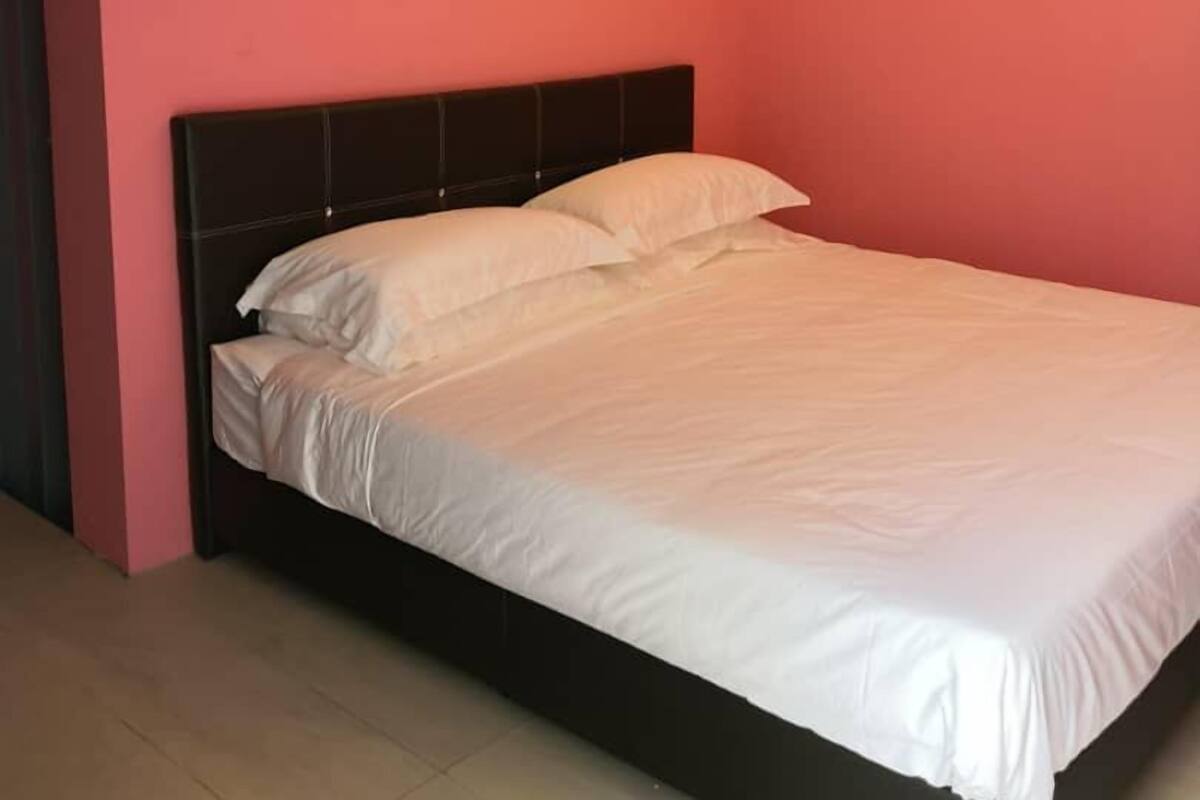 A bedroom with a bed against a pink wall, a black headboard, and a visible door on the left.