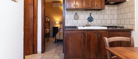 A kitchen with wooden cabinets, a sink, and a stove. There is a chair and a table in the room.