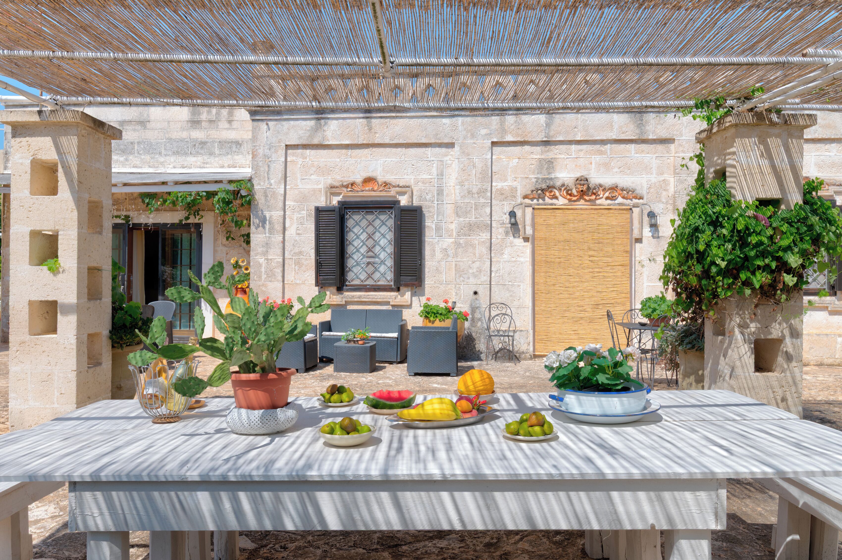 An outdoor dining area with a table set for a meal, surrounded by potted plants and a stone wall.