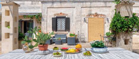An outdoor dining area with a table set for a meal, surrounded by potted plants and a stone wall.