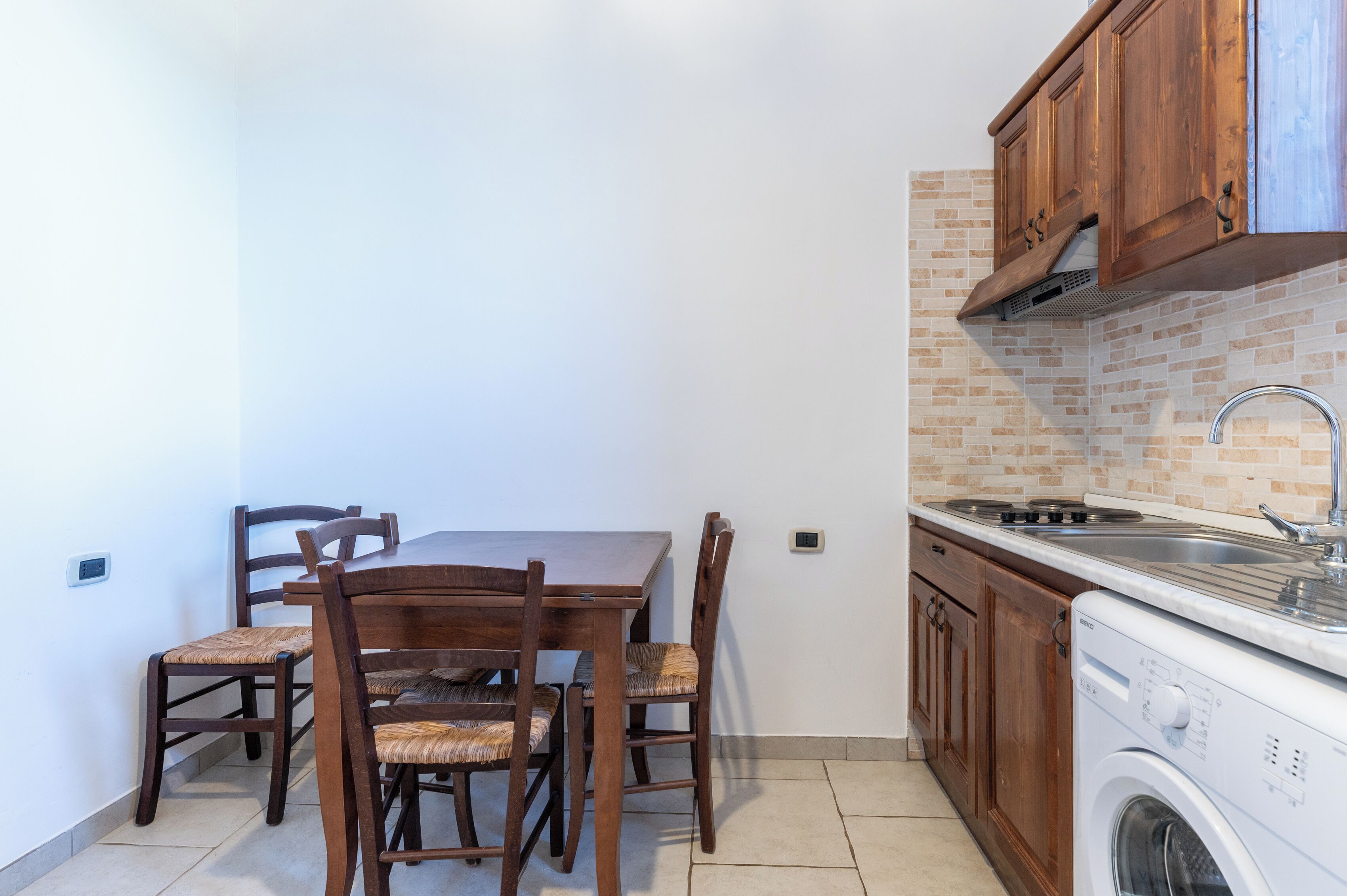 A compact kitchen with a dining table, chairs, a washing machine, and wooden cabinets.