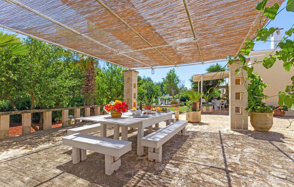 An outdoor patio with wooden tables and benches, surrounded by potted plants and a pergola.