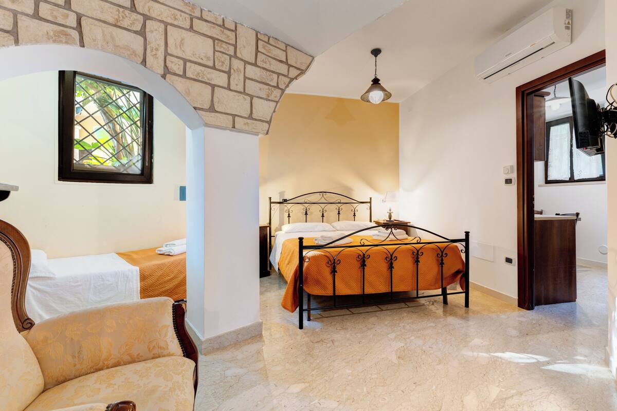 Une chambre avec un lit, une chaise, une fenêtre et un mur en pierre.