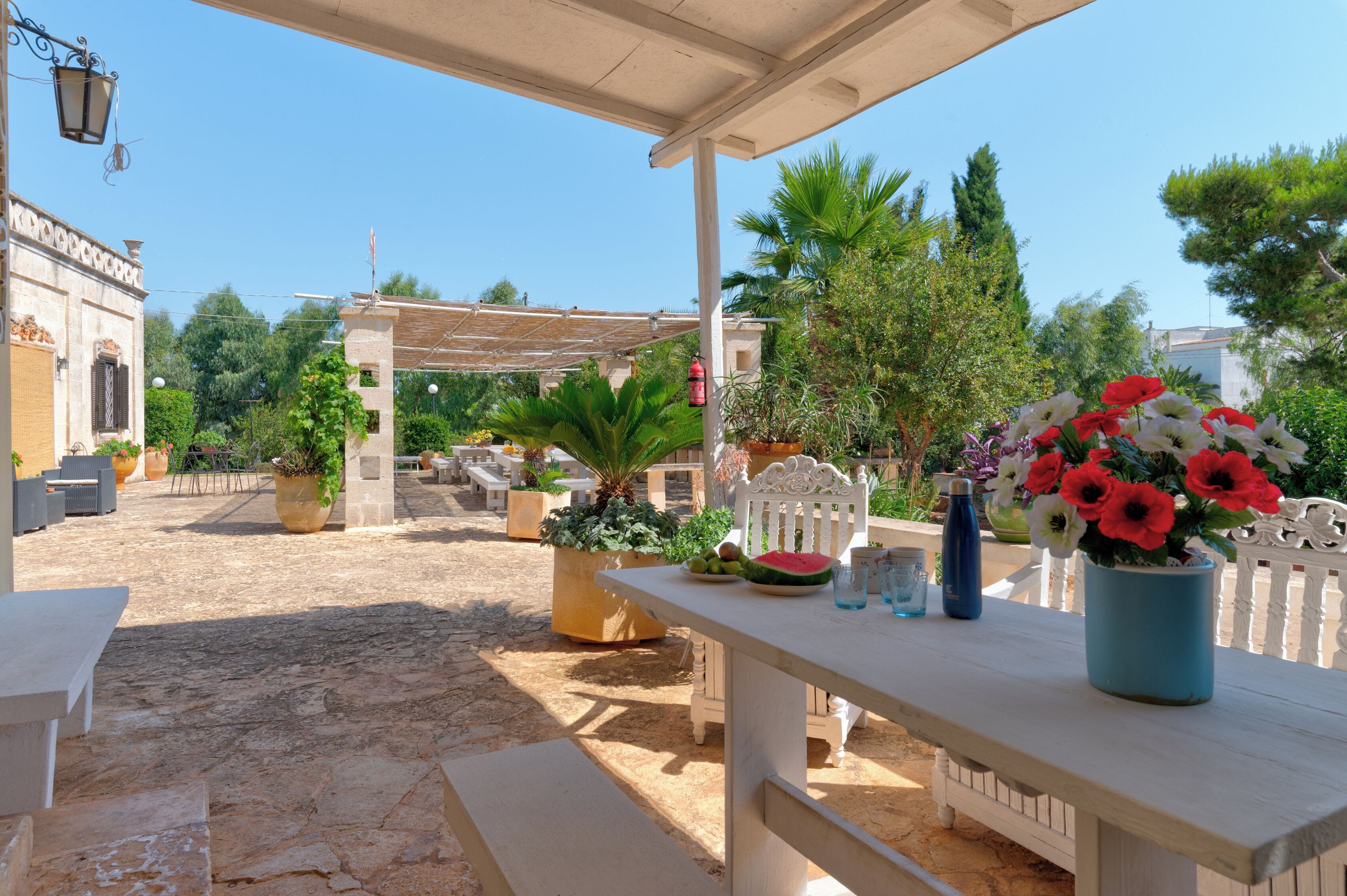 An outdoor patio area with stone flooring, white furniture, and potted plants.