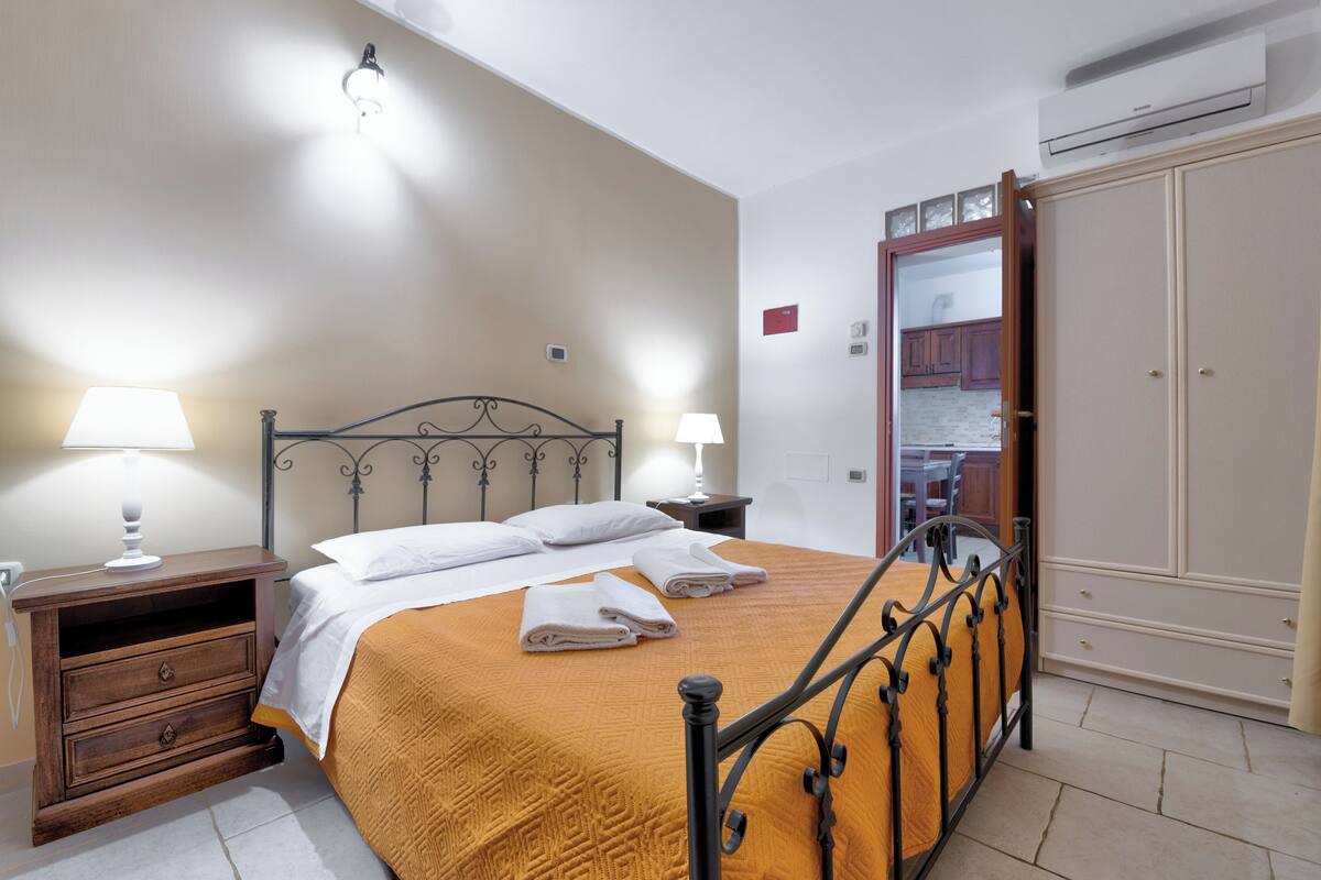 Un lit bien fait, avec une tête de lit, deux tables de chevet avec des lampes, une armoire et un appareil de climatisation.