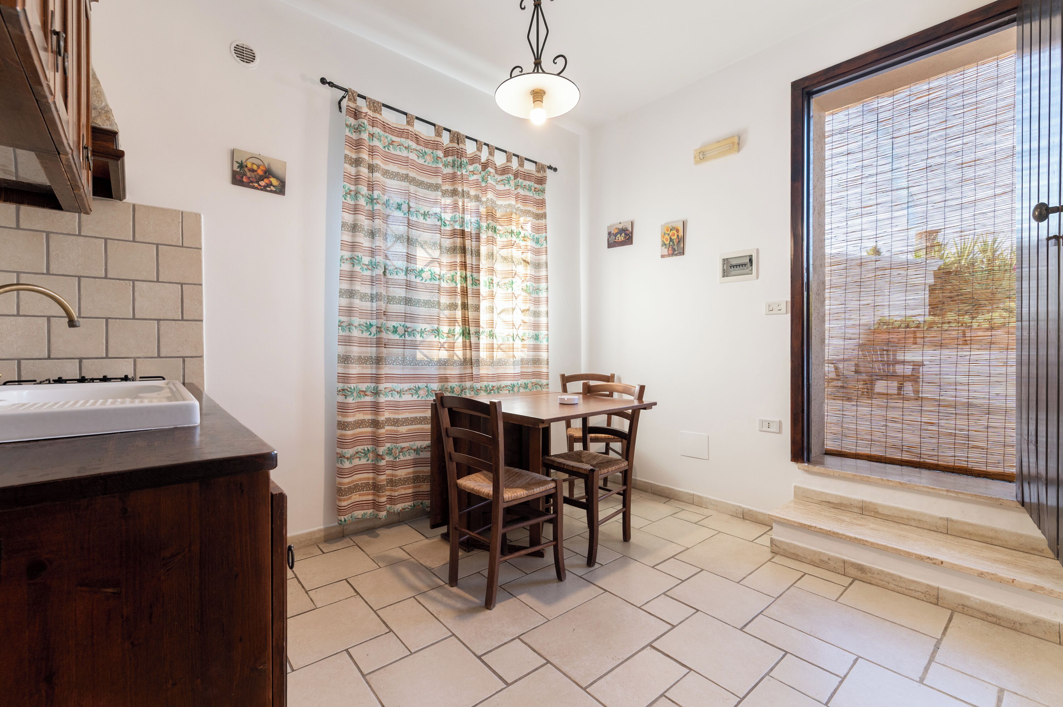 A kitchen with a countertop, a dining table with chairs, a window with a curtain, and a view of the outside.