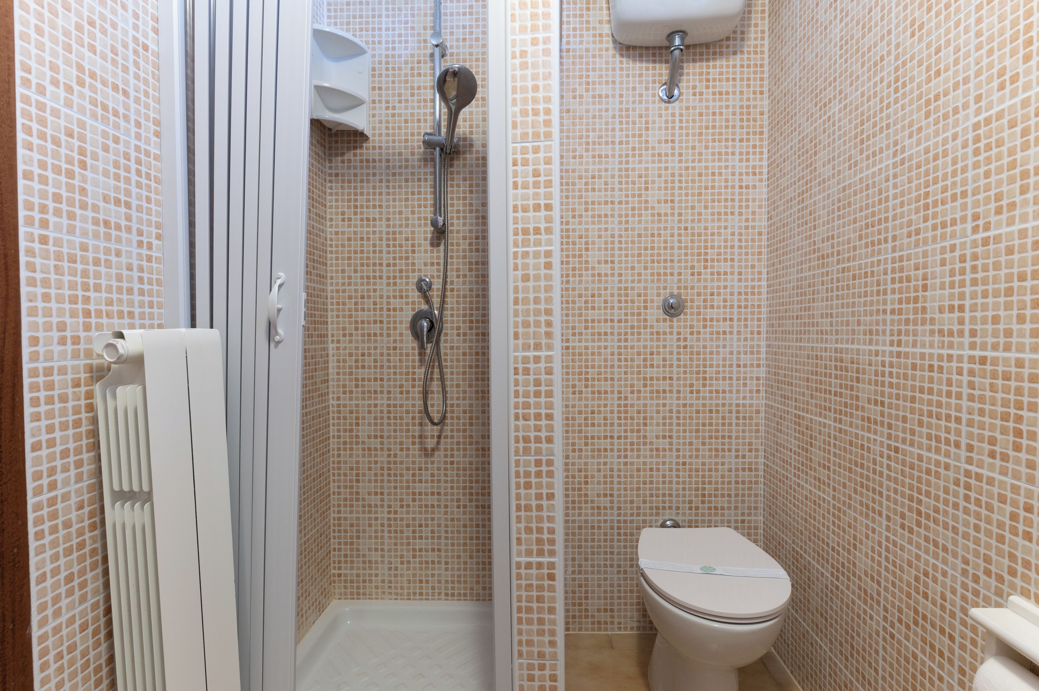 A small bathroom with a shower, toilet, and a radiator.