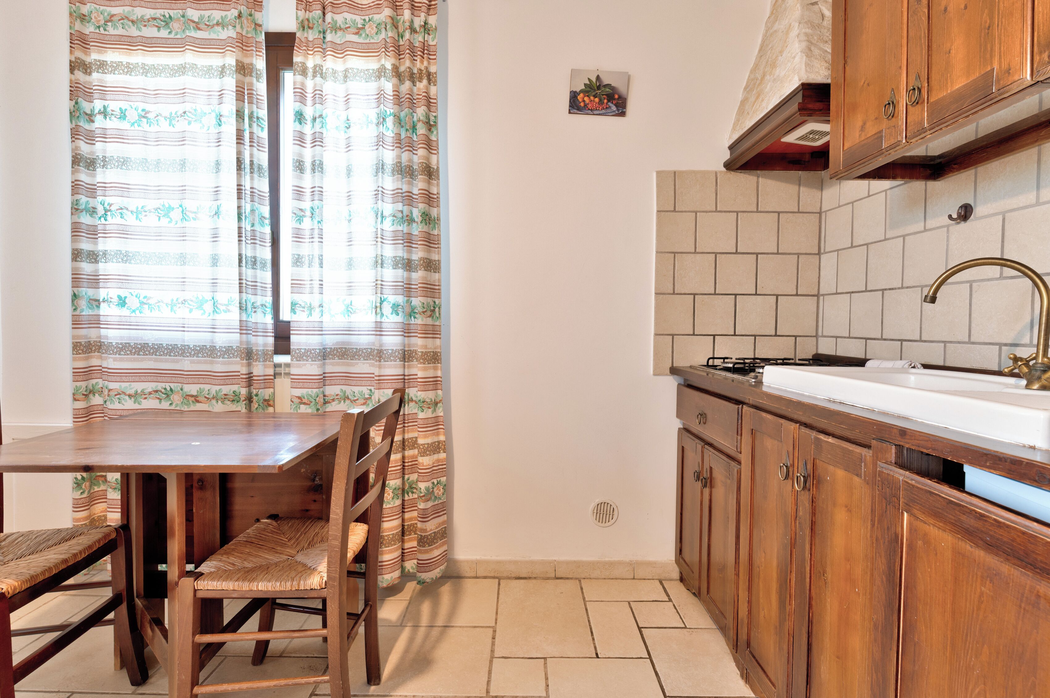 Una cocina compacta con armarios de madera, un lavamanos blanco y una ventana con cortinas a rayas.