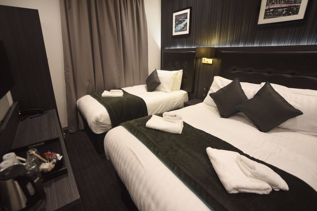 A hotel room with two beds, a TV, a desk with a kettle, and a framed picture on the wall.
